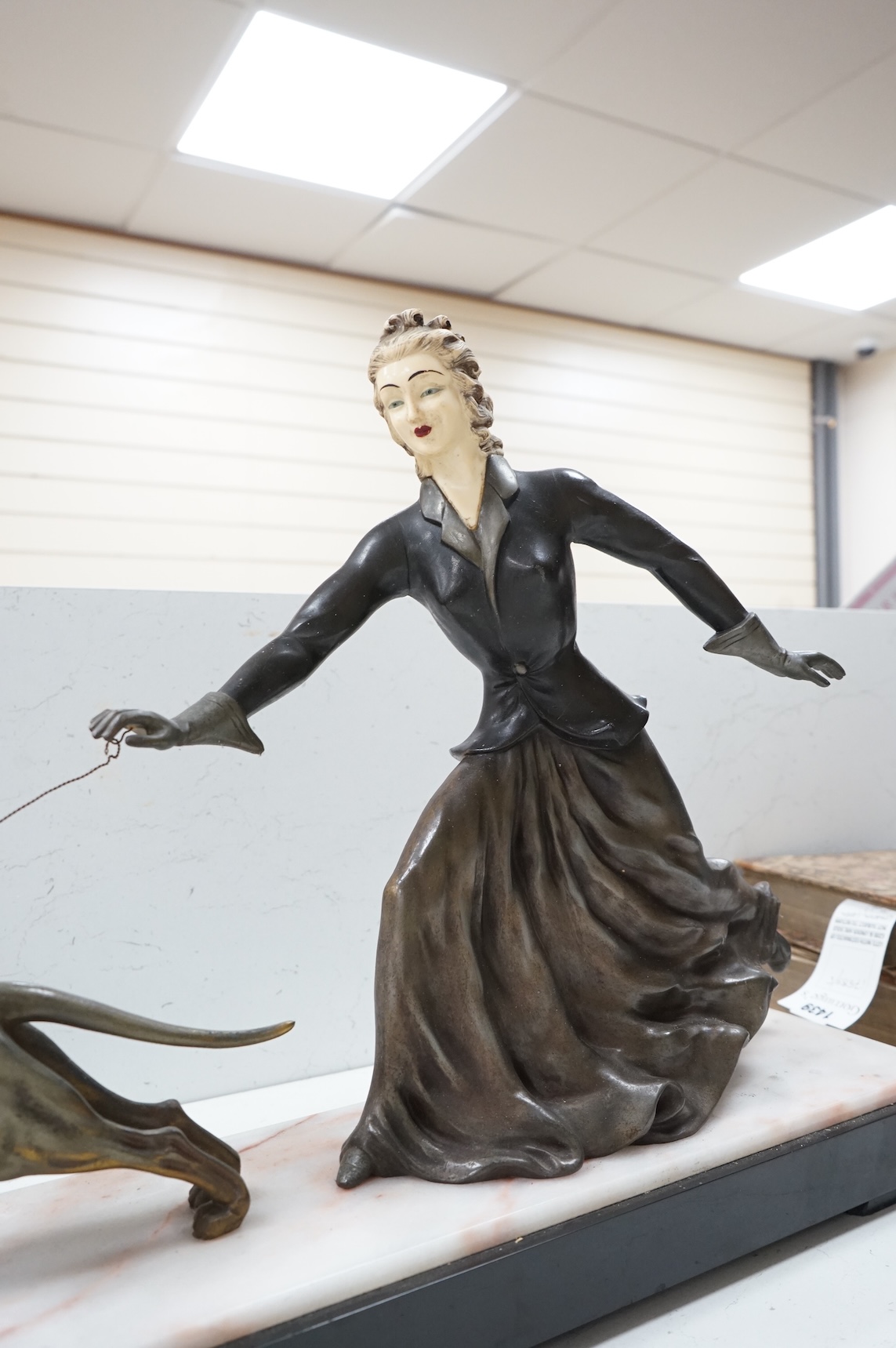 An Art Deco French spelter and ivorine model ‘Walkies Lady and Dog’, on a black marble and cream onyx base, 75cm long